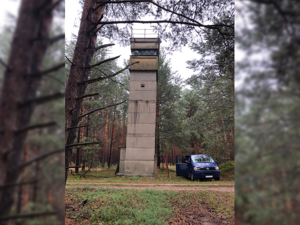 Beobachtungsturm aus Beton im Wald, daneben blauer VW-Bus
