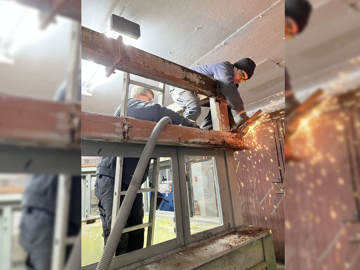 zwei Männer in Stahlkabine arbeiten mit Flex-Maschine, Funken sprühen