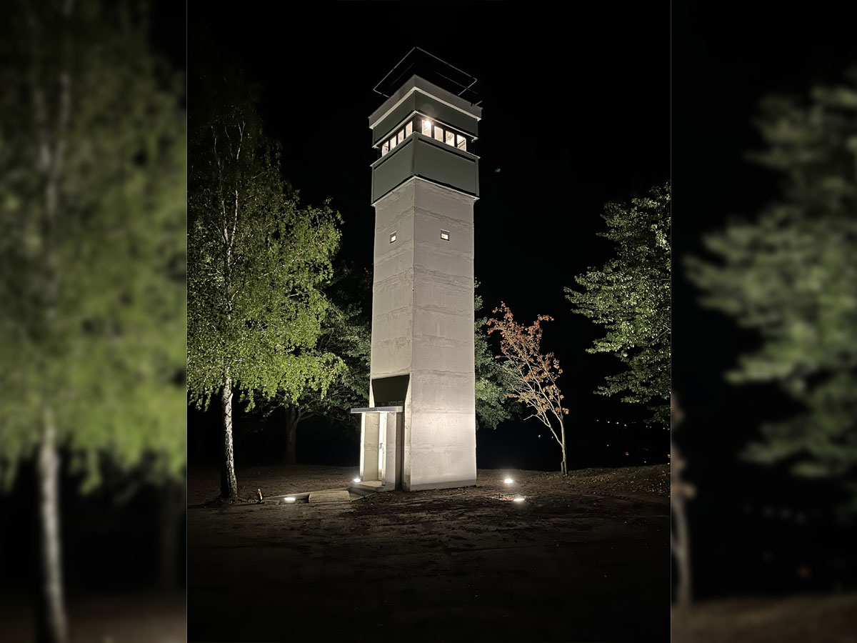 Fertig aufgebauter Beobachtungsturm bei Nacht, angestrahlt von vier Scheinwerfern im Boden.