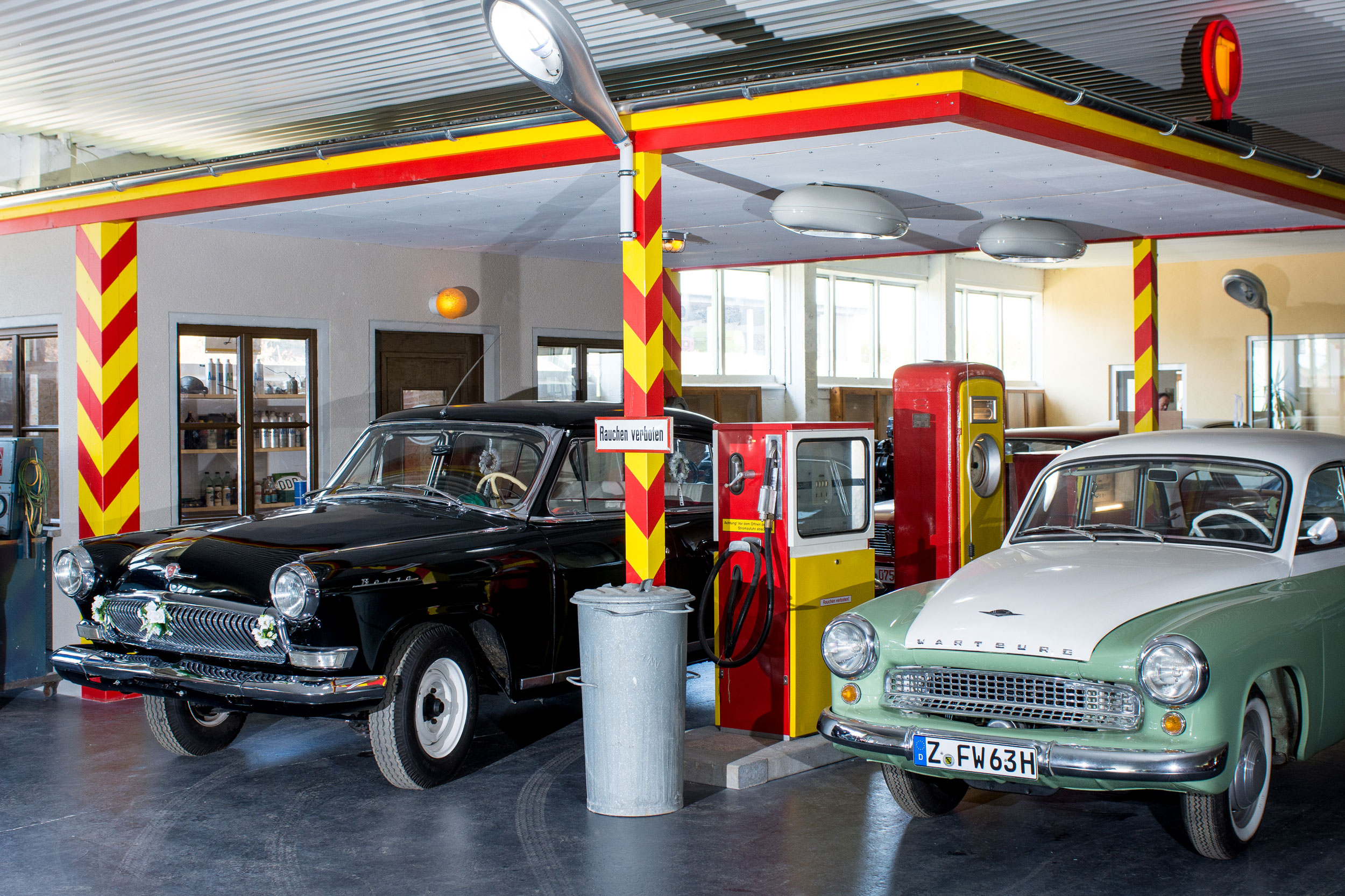 Alte Tankstelle im Oldtimer-Museum mit einem schwarzen und einem weiß-cremefarbenen Oldtimer davor